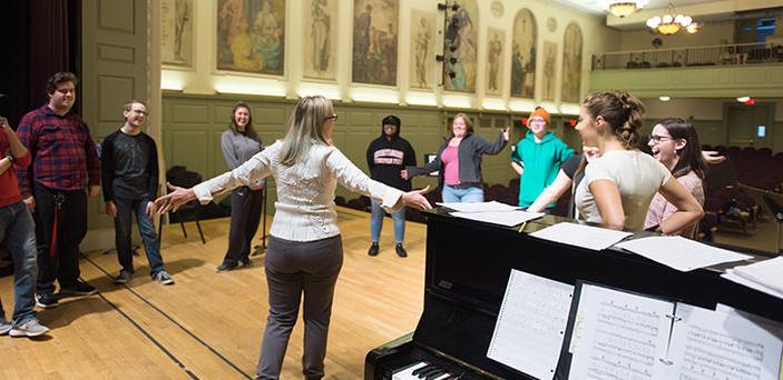 BSU professor forms a circle on stage with students next to her piano